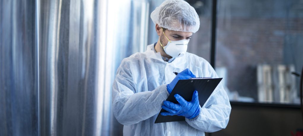 Concentrated technologist expert in white suit controlling production in food factory.